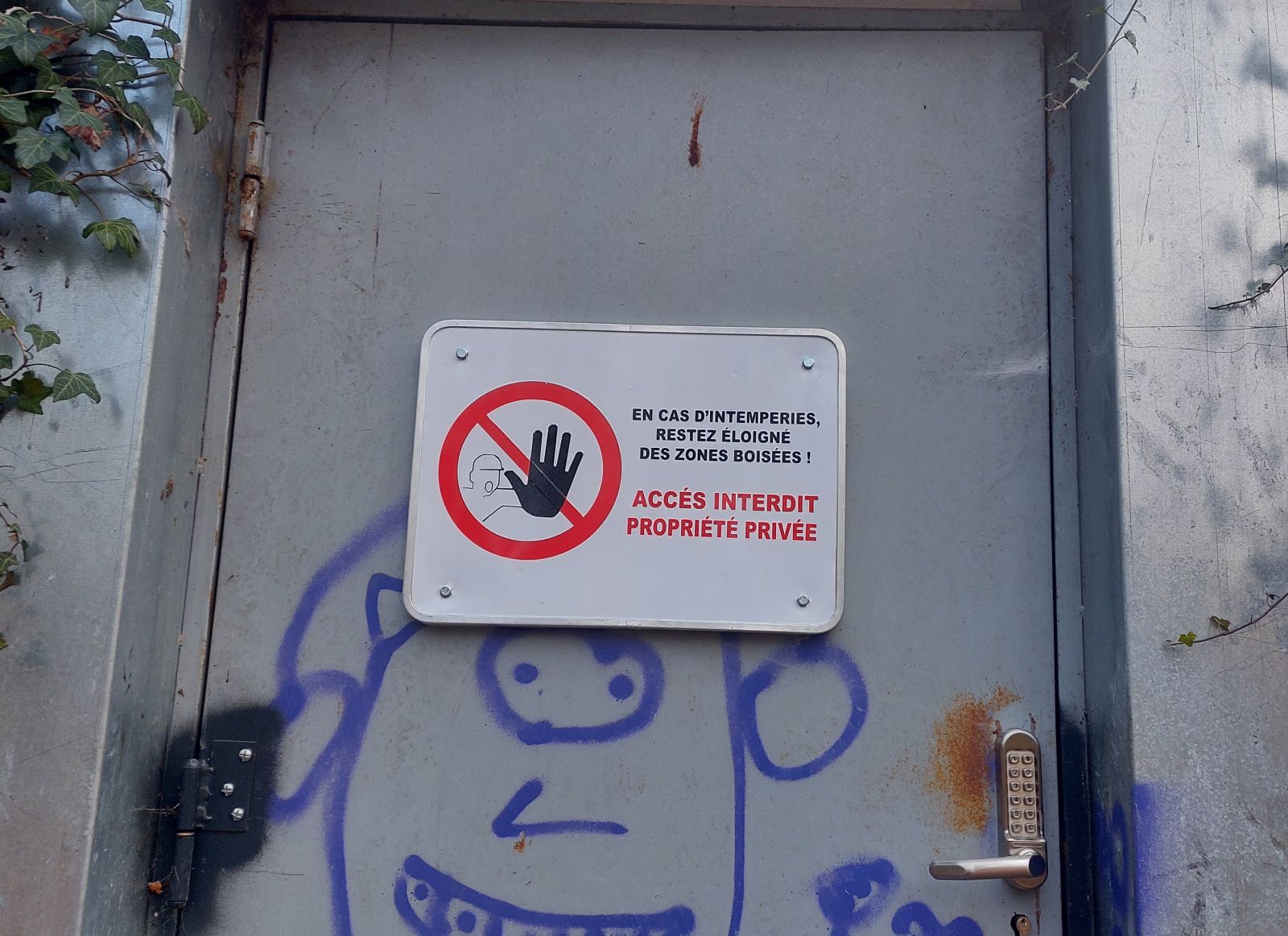 Panneau de signalétique en tôle retournée avec découpe vinyle rouge et noir sur fond blanc.